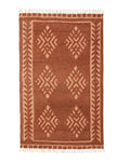 A rectangular, flatweave rug with a warm rust color, featuring geometric patterns and fringed edges.